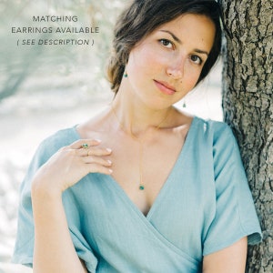 Puede incluir: Una mujer con un vestido azul claro con un collar de oro y un colgante de piedra preciosa verde. Tambi&eacute;n lleva un anillo de oro con una piedra preciosa verde. El texto "MATCHING EARRINGS AVAILABLE ( SEE DESCRIPTION )" es visible en la parte superior de la imagen.