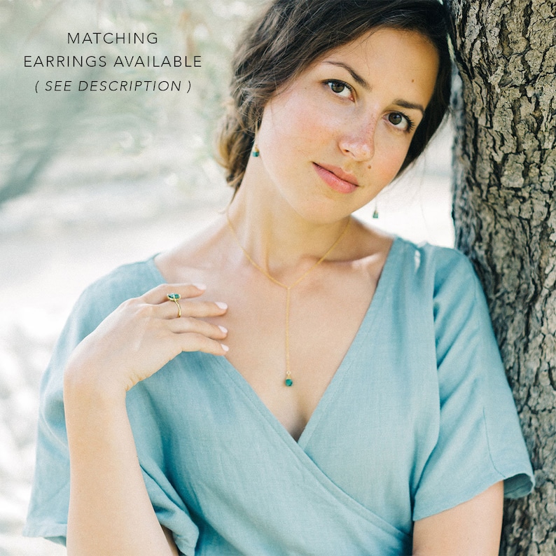 Puede incluir: Una mujer con un vestido azul claro con un collar de oro y un colgante de piedra preciosa verde. Tambi&eacute;n lleva un anillo de oro con una piedra preciosa verde. El texto "MATCHING EARRINGS AVAILABLE ( SEE DESCRIPTION )" es visible en la parte superior de la imagen.