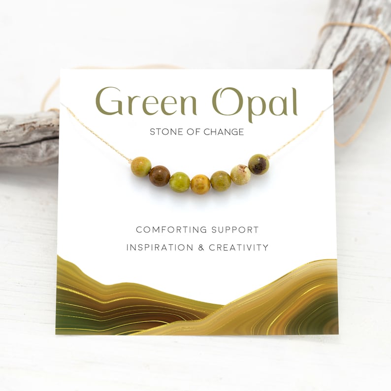 Puede incluir: Una tarjeta con el texto "Green Opal, Stone of Change, Comforting Support, Inspiration & Creativity" y una cadena dorada con cuentas de &oacute;palo verde.