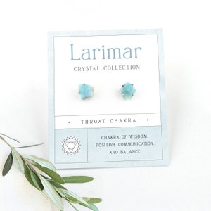 以下が含まれることがあります： 白いカードに、薄い水色のラリマーのクリスタル製のイヤリングが2つ並んでいます。カードには「Larimar Crystal Collection」と「Throat Chakra」の文字が書かれており、「Chakra of Wisdom. Positive Communication. And Balance.」の文字も書かれています。