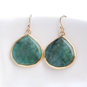May include: A pair of gold-toned dangle earrings with large, teardrop-shaped emerald green stones.