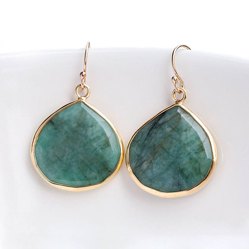 May include: A pair of gold-toned dangle earrings with large, teardrop-shaped emerald green stones.
