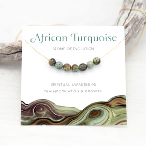 May include: A card with the text "African Turquoise" and "Stone of Evolution" with a gold chain and green beads. The card also says "Spiritual Awakening, Transformation & Growth".