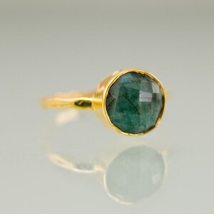 Pode incluir: Um anel de ouro com uma gema verde escura. O anel tem uma banda simples e a gema est&aacute; engastada em um engaste de bezel.