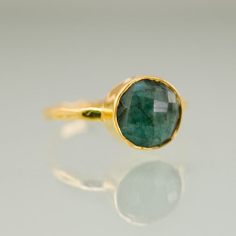 Pode incluir: Um anel de ouro com uma gema verde escura. O anel tem uma banda simples e a gema est&aacute; engastada em um engaste de bezel.