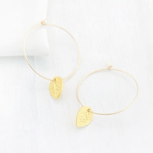 May include: Gold hoop earrings with a leaf charm hanging from each hoop.