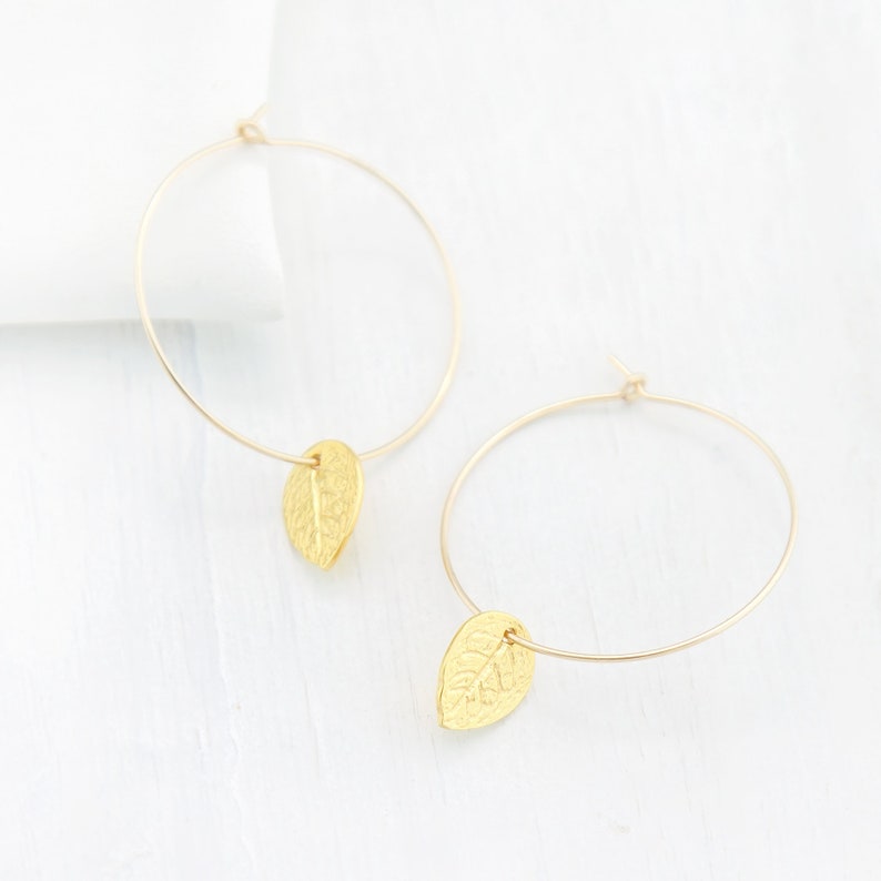 May include: Gold hoop earrings with a leaf charm hanging from each hoop.