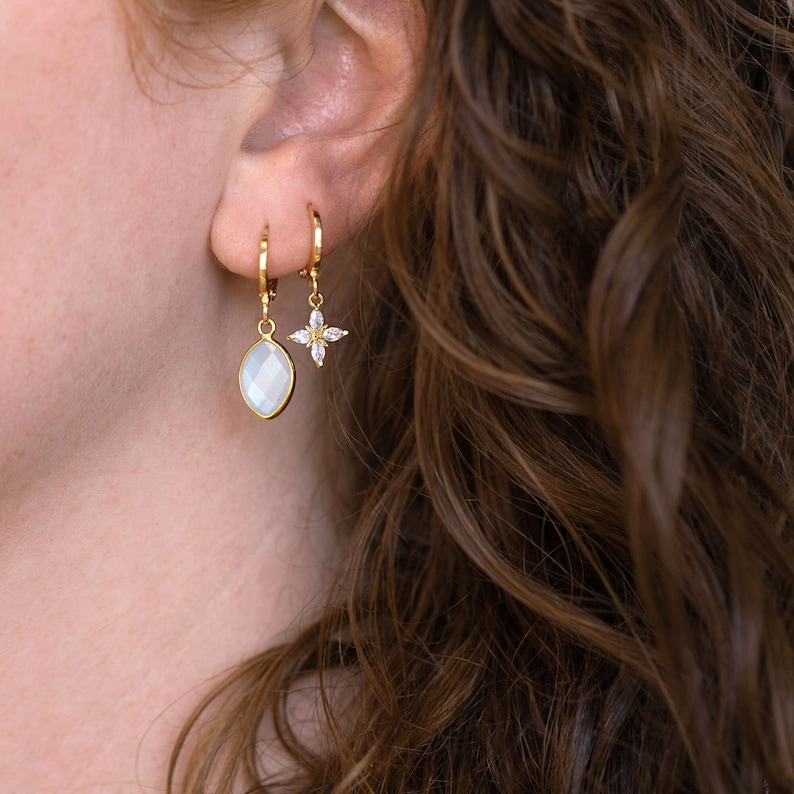 May include: Gold hoop earrings with a white gemstone dangle and a small gold flower charm with clear stones.