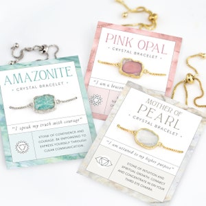 Pu&ograve; includere: Tre braccialetti di cristallo con catene dorate e ciondoli di pietre preziose. I braccialetti sono esposti su carte con i nomi "Pink Opal", "Mother of Pearl" e "Amazonite" e le loro affermazioni del chakra corrispondenti.