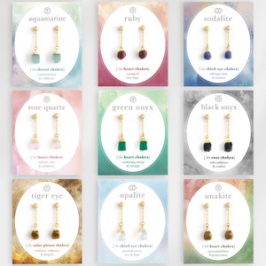 以下が含まれることがあります： 異なる色の宝石が付いた金のイヤリングが9組。各ペアは、宝石の名前と対応するチャクラが書かれたカードに表示されています。宝石はアクアマリン、ルビー、ソーダライト、ローズクォーツ、グリーンオニキス、ブラックオニキス、タイガーアイ、オパール、ウnakiteです。