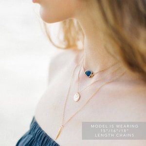 May include: A model is wearing three gold necklaces with a blue stone pendant, a gold disc pendant, and a long gold pendant. The text on the image reads "MODEL IS WEARING 15"/16"/18" LENGTH CHAINS".