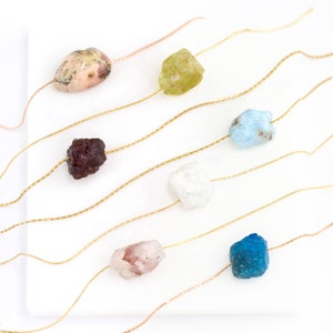 Peut inclure: Sept pierres précieuses de différentes couleurs enfilées sur des cordons dorés. Les pierres précieuses sont roses, vertes, bleues, brunes, blanches, roses et bleues.
