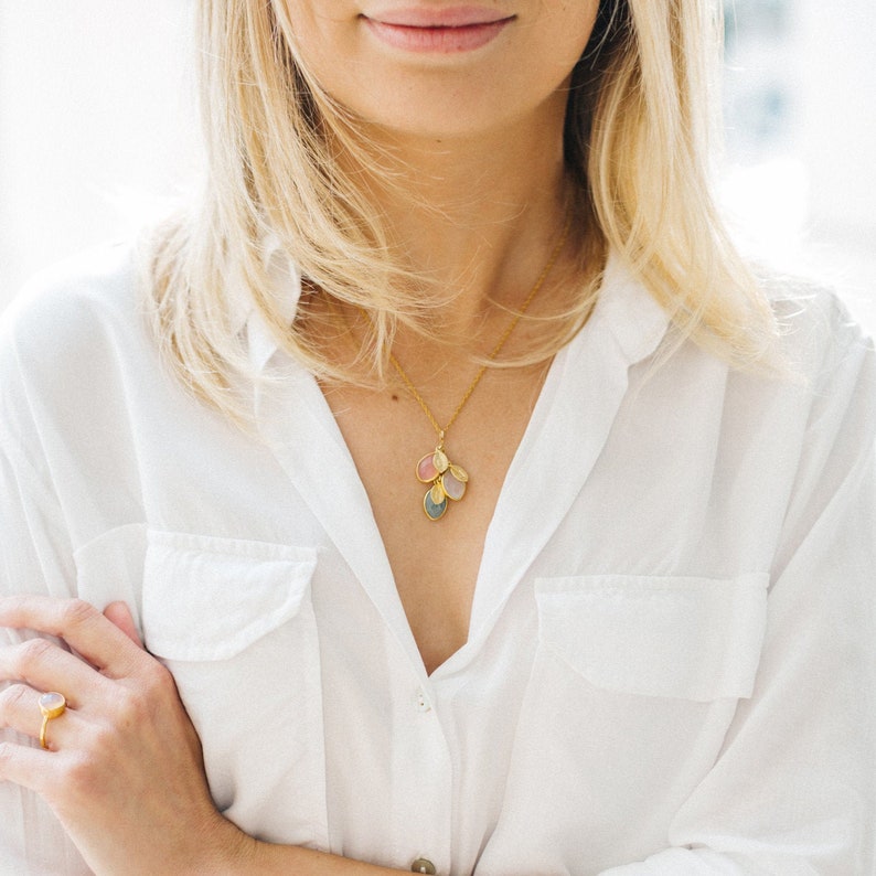 May include: A gold necklace with a cluster of five oval-shaped stones in shades of pink, blue, and gray.