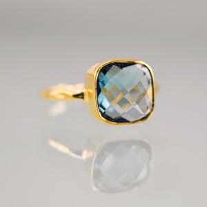 Op de afbeelding: Een gouden ring met een grote, vierkante blauwe edelsteen.