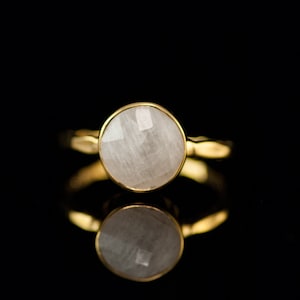 Puede incluir: Un anillo de oro con una piedra preciosa blanca. La piedra es redonda y tiene un corte facetado.