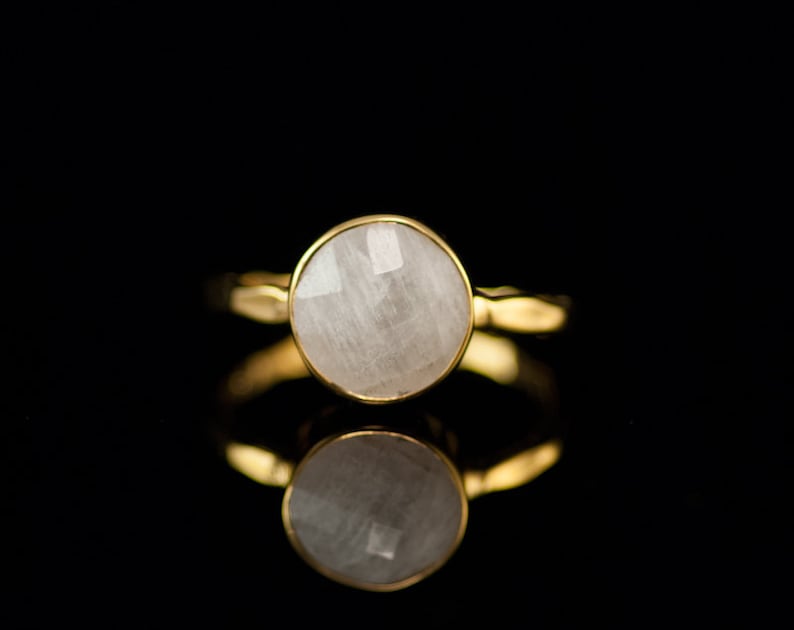 Puede incluir: Un anillo de oro con una piedra preciosa blanca. La piedra es redonda y tiene un corte facetado.