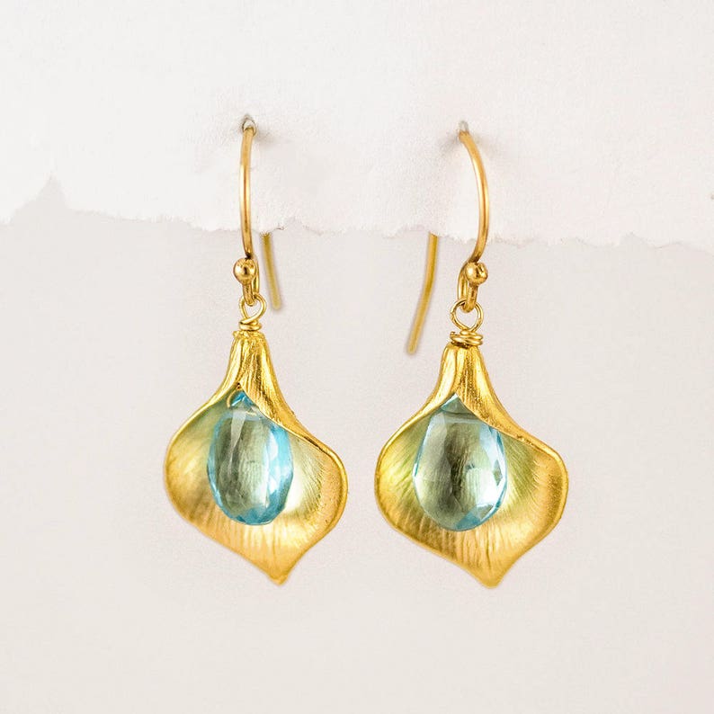 May include: Gold earrings with a blue teardrop-shaped gemstone set in a gold flower design.