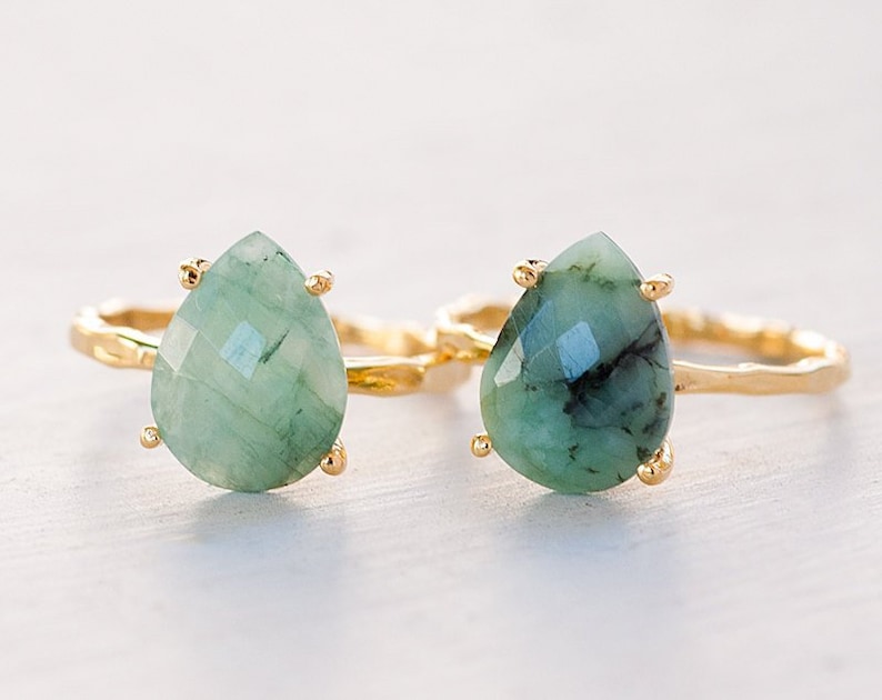 May include: Two gold rings with teardrop-shaped green gemstone settings. The rings have a twisted band design.