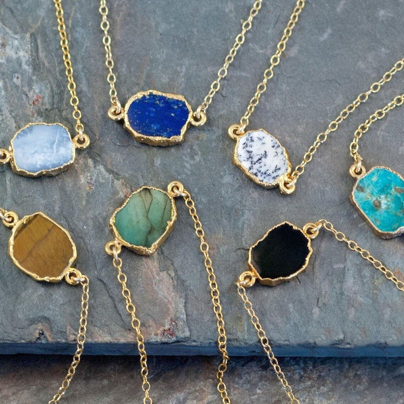 May include: A set of seven gold chain necklaces with different colored gemstone pendants. The pendants are all irregular in shape and have a gold rim. The gemstones are blue, white, green, brown, black, and turquoise.