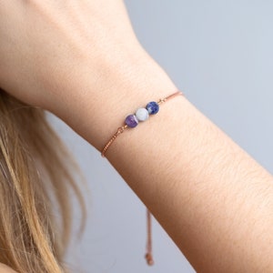May include: A delicate rose gold chain bracelet with three gemstone beads: amethyst, white agate, and blue sodalite.