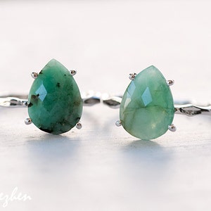 May include: Two silver rings with pear-shaped green gemstone settings. The rings are on a white surface.
