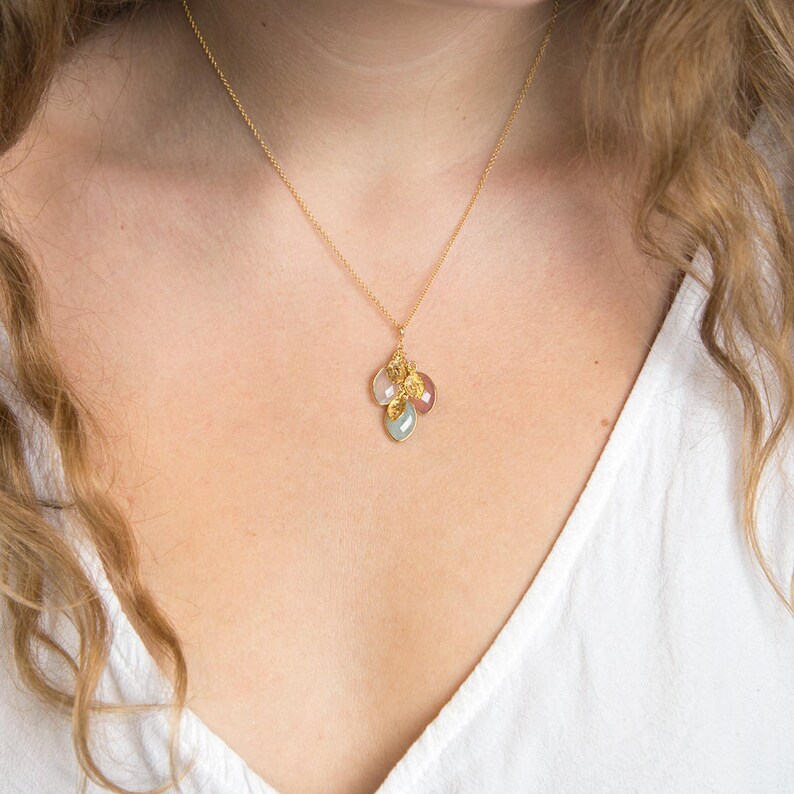 May include: A gold chain necklace with a pendant featuring a cluster of small, colorful gemstones. The pendant is made of gold and has a delicate, feminine design.