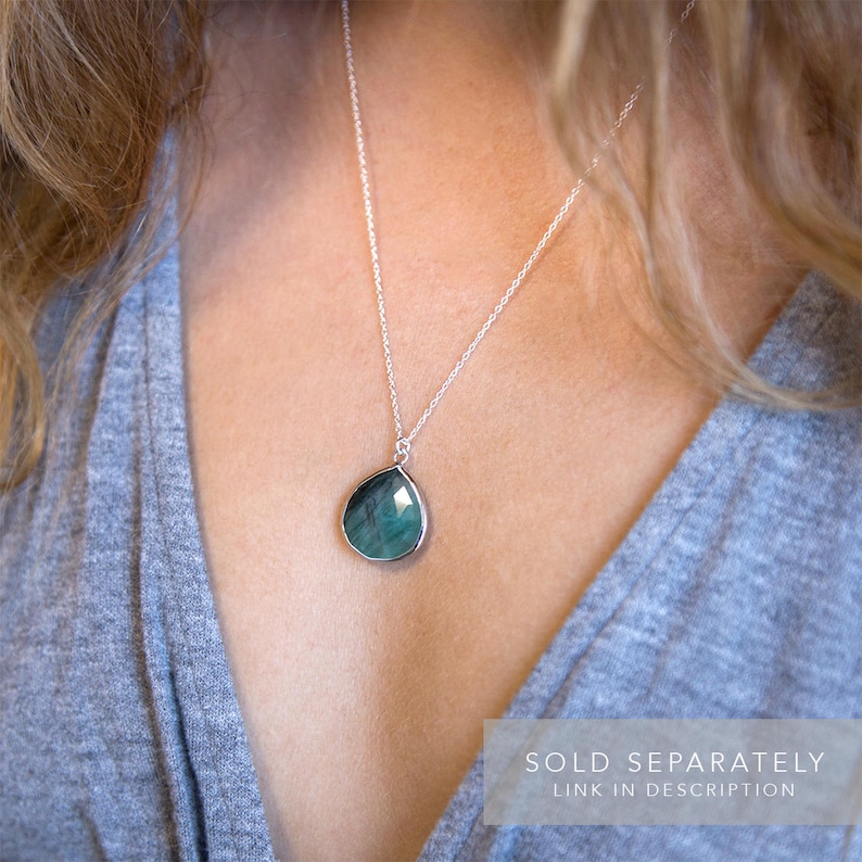 May include: A silver chain necklace with a teardrop-shaped green gemstone pendant.