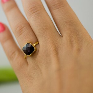 K&ouml;nnte beinhalten: Ein goldener Ring mit einem quadratischen schwarzen Edelstein.