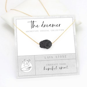 以下が含まれることがあります： 黒い溶岩石のペンダントが付いた金のチェーンネックレス。カードには「The Dreamer Archetype Crystal Collection Lava Stone Embrace Your Hopeful Spirit」と書かれています。