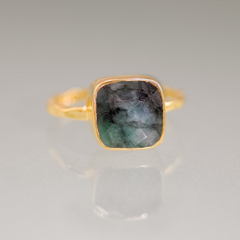 K&ouml;nnte beinhalten: Ein goldener Ring mit einem quadratischen smaragdgr&uuml;nen Edelstein.