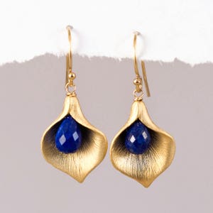 Puede incluir: Pendientes de oro con una piedra preciosa azul en forma de flor.