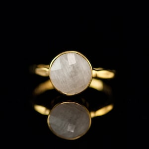 May include: A gold ring with a white gemstone. The ring is set in a simple band and the gemstone is round and faceted.