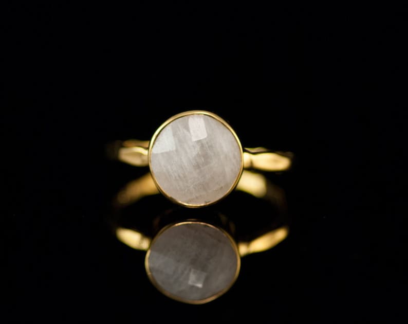 May include: A gold ring with a white gemstone. The ring is set in a simple band and the gemstone is round and faceted.