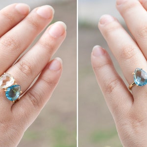 May include: Two teardrop-shaped rings with gold settings. The ring on the left has a clear stone, and the ring on the right has a light blue stone.