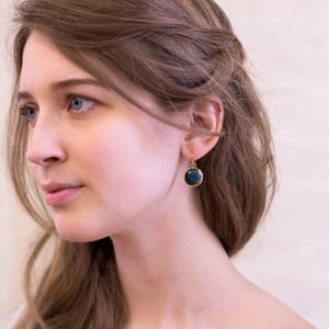 May include: A pair of gold dangle earrings with a round, dark blue gemstone.