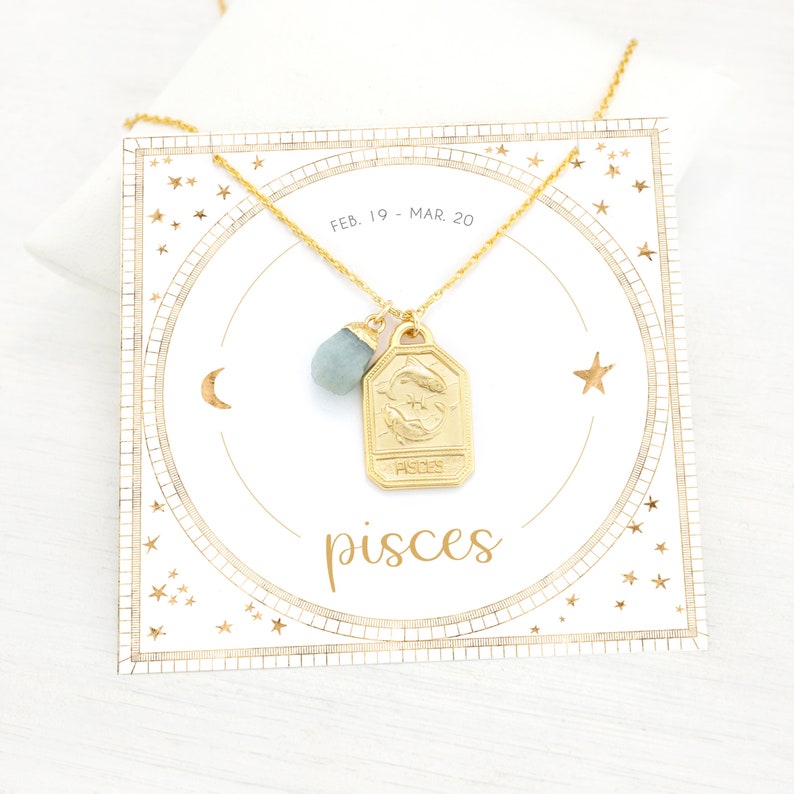 May include: Gold necklace with a Pisces zodiac sign charm and a light blue gemstone pendant. The necklace is displayed on a white card with a gold star and crescent moon design. The card also includes the text "FEB. 19 - MAR. 20" and "pisces".