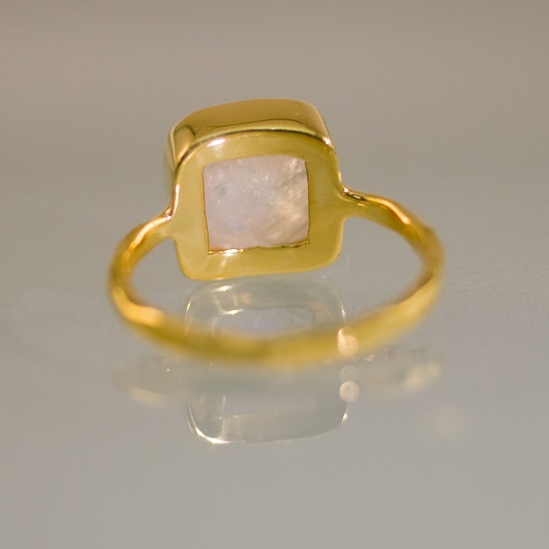 May include: A gold ring with a square-shaped moonstone set in the center.