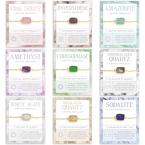 Pu&ograve; includere: Un set di dieci braccialetti di cristallo, ognuno con un tipo di cristallo diverso e un'affermazione corrispondente. I braccialetti sono esposti su uno sfondo bianco con uno schema di colori rosa, verde, blu e grigio. Ogni braccialetto ha una catena dorata e un ciondolo di cristallo rettangolare.