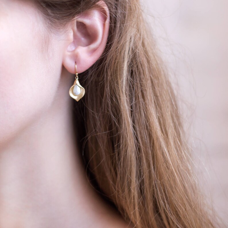 Puede incluir: Pendientes de oro con una delicada perla blanca. Los pendientes tienen forma de p&eacute;talo de flor.