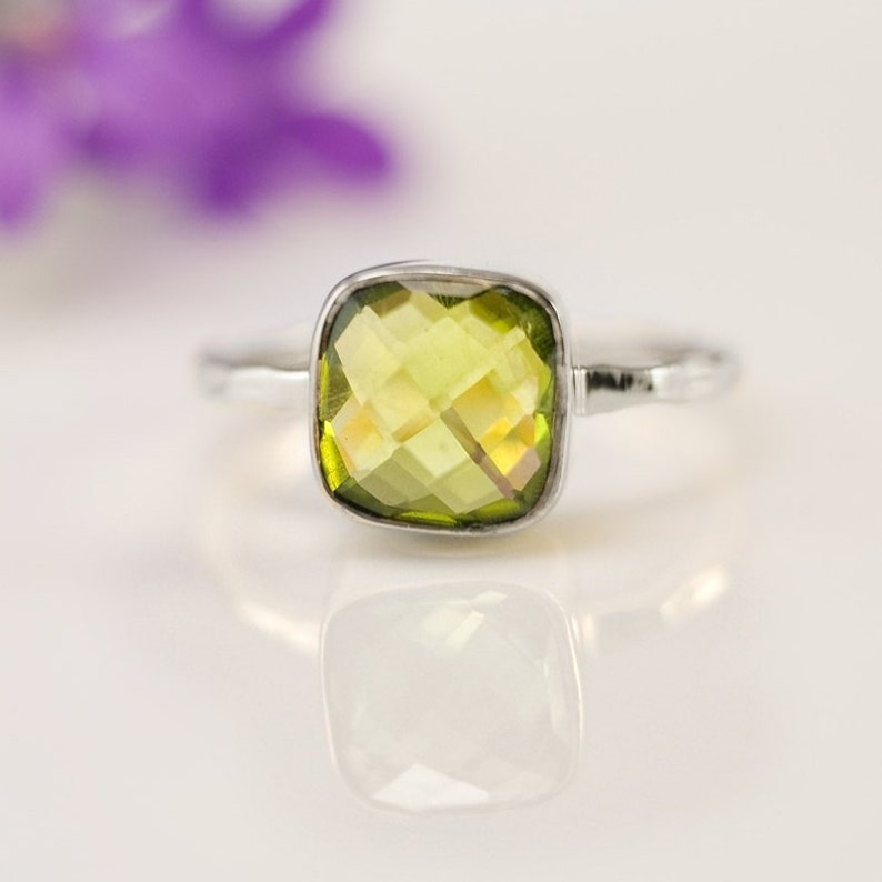 May include: A silver ring with a square, faceted, green gemstone.