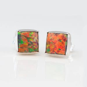 Pu&ograve; includere: Un paio di orecchini a bottone quadrati in argento con una pietra di opale colorata in ogni orecchino. Le pietre di opale hanno una miscela di colori arancio, rosso, verde e nero.