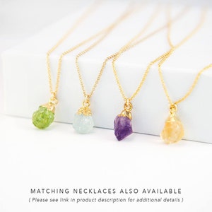 May include: Four gold necklaces with different colored gemstone pendants. The pendants are in the shape of rough, natural crystals. From left to right, the gemstones are green, light blue, purple, and orange.
