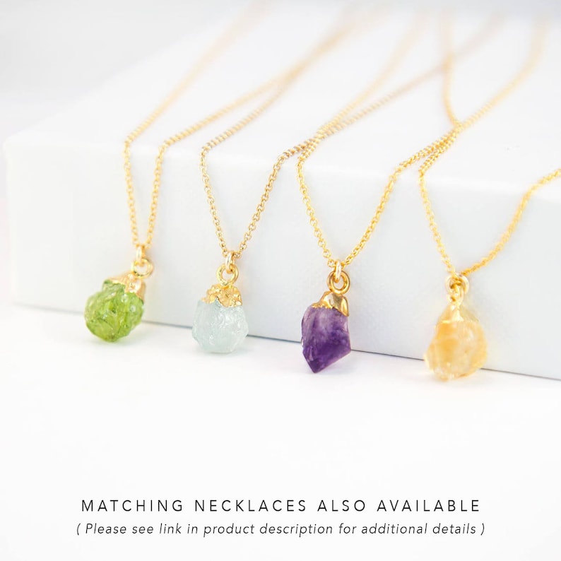 May include: Four gold necklaces with different colored gemstone pendants. The pendants are in the shape of rough, natural crystals. From left to right, the gemstones are green, light blue, purple, and orange.