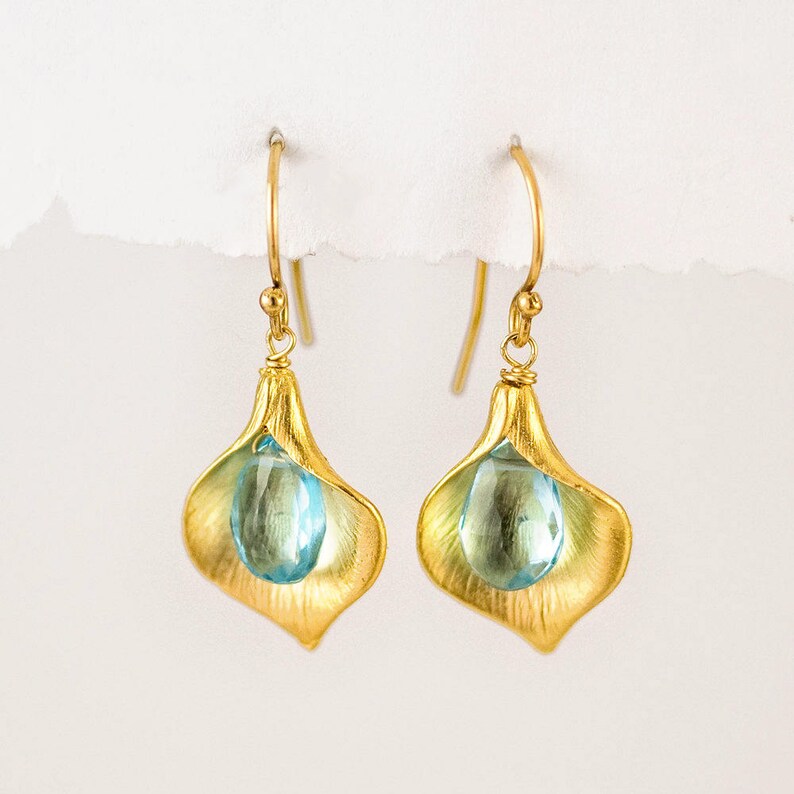 Puede incluir: Pendientes de oro con una piedra preciosa azul en forma de l&aacute;grima engastada en un dise&ntilde;o de flor de oro.
