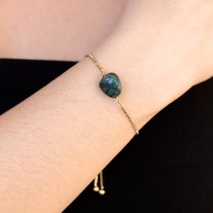 May include: A gold chain bracelet with a dark green gemstone pendant. The bracelet has an adjustable sliding clasp.
