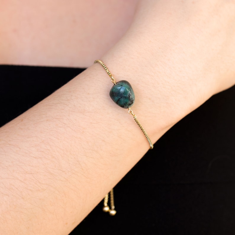 May include: A gold chain bracelet with a dark green gemstone pendant. The bracelet has an adjustable sliding clasp.