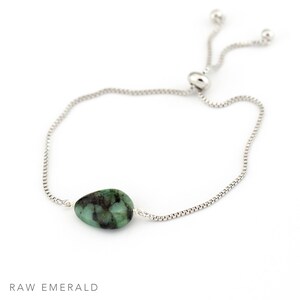 May include: A silver chain bracelet with a raw emerald gemstone. The bracelet has an adjustable sliding clasp.