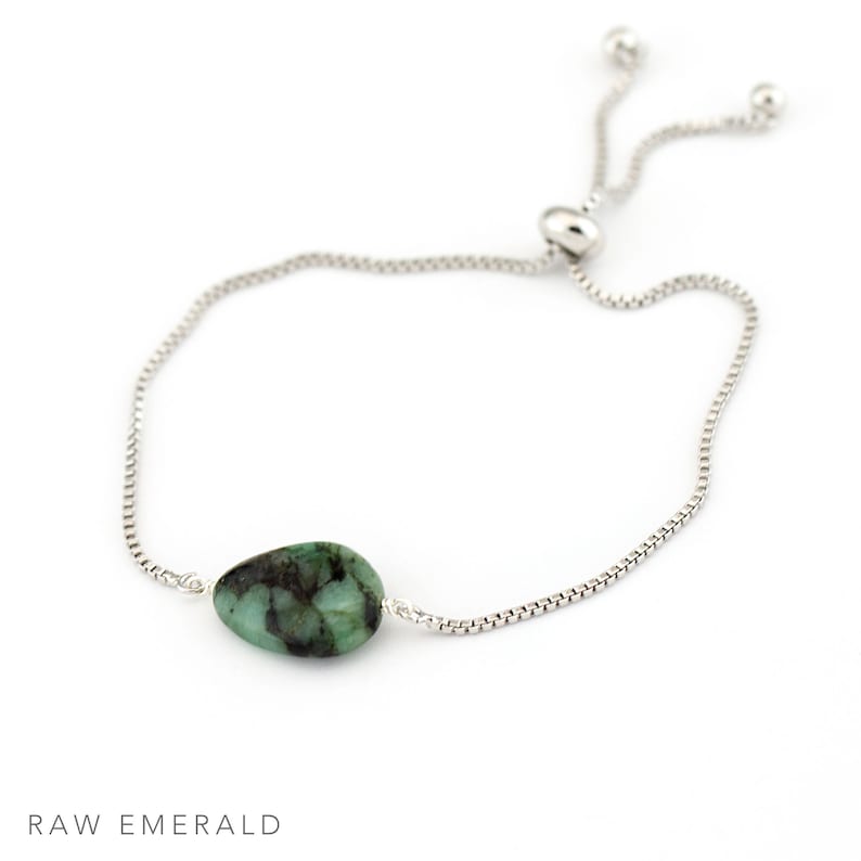 May include: A silver chain bracelet with a raw emerald gemstone. The bracelet has an adjustable sliding clasp.