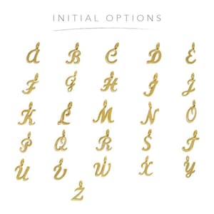 Pode incluir: Um conjunto de 26 pingentes de letras cursivas douradas, cada letra do alfabeto &eacute; exibida em um quadrado separado. As letras est&atilde;o em um estilo de fonte cursivo. As letras est&atilde;o organizadas em ordem alfab&eacute;tica.