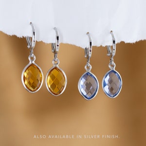 May include: Three pairs of dangle earrings with silver hoops and teardrop-shaped crystal stones. The stones are in shades of amber and blue.